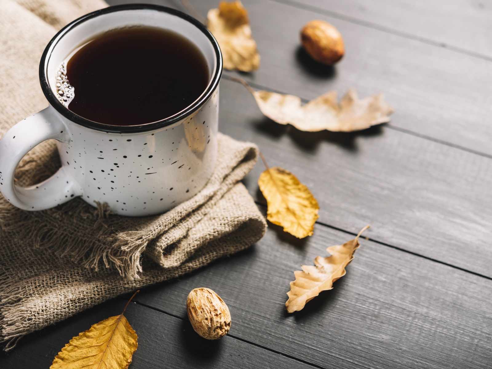 Кружка кофе на столе с листьями и пледом