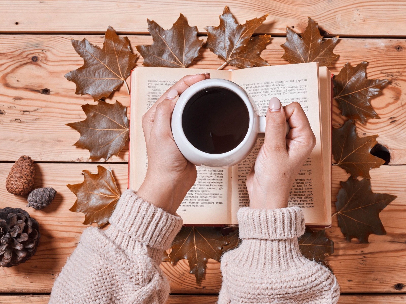 Чашка кофе в руках на столе с книгой и листьями