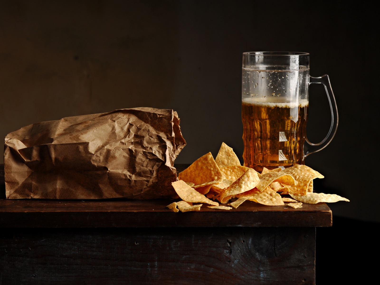 Бокал пива с чипсами в пакете на столе