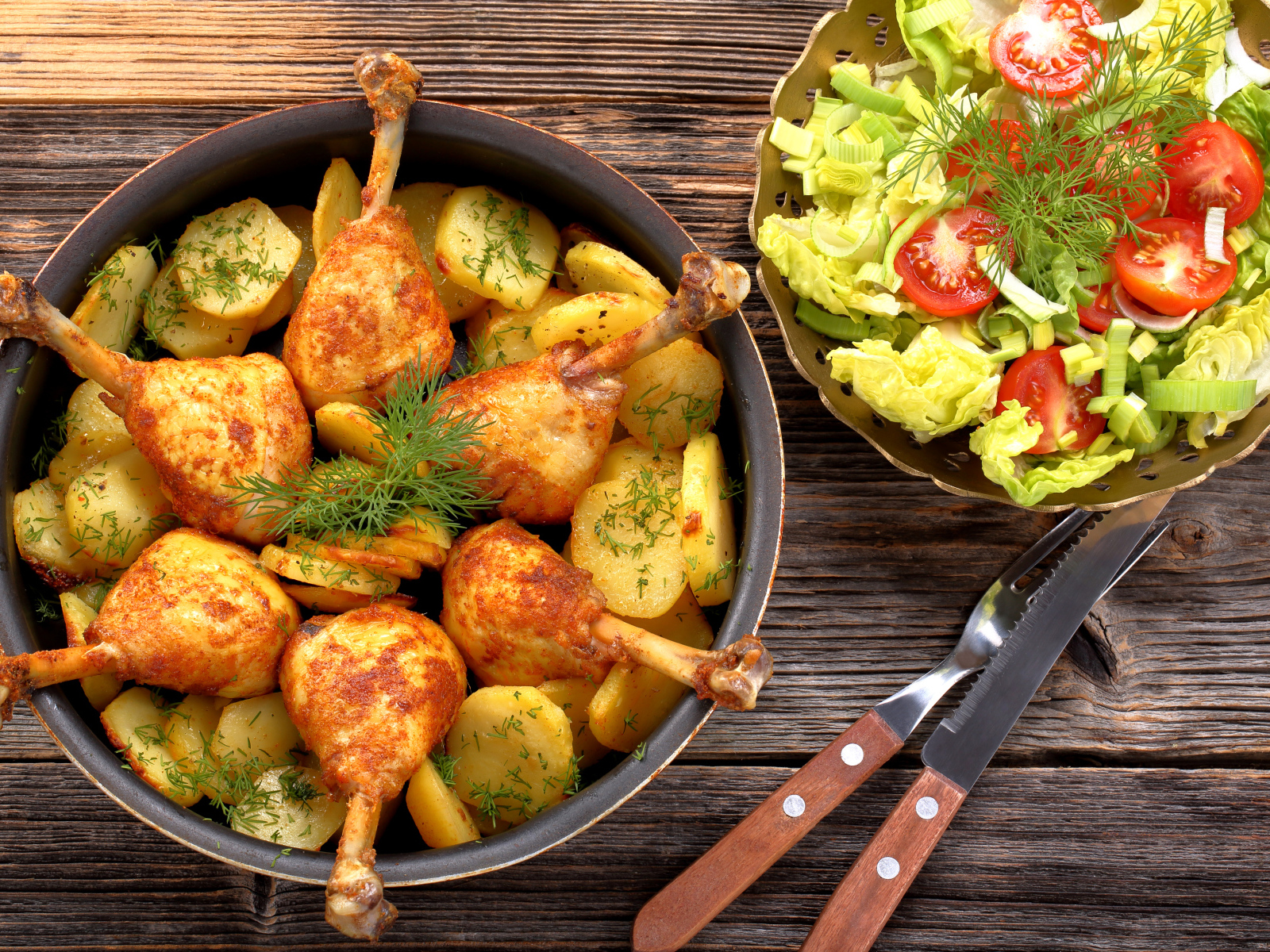 Fried chicken legs with potatoes on a table with salad