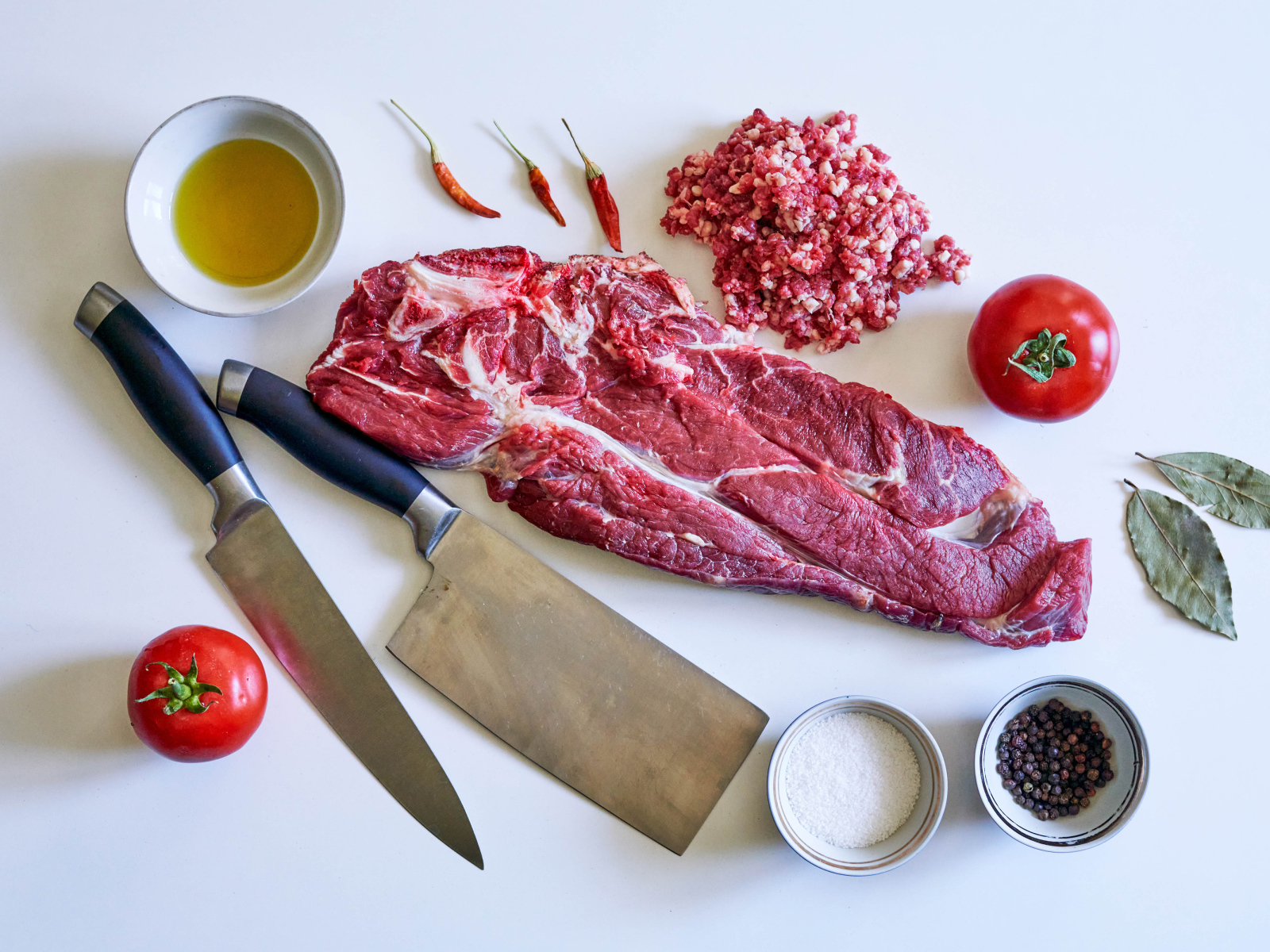 Кусок мяса со специями и ножами на столе 