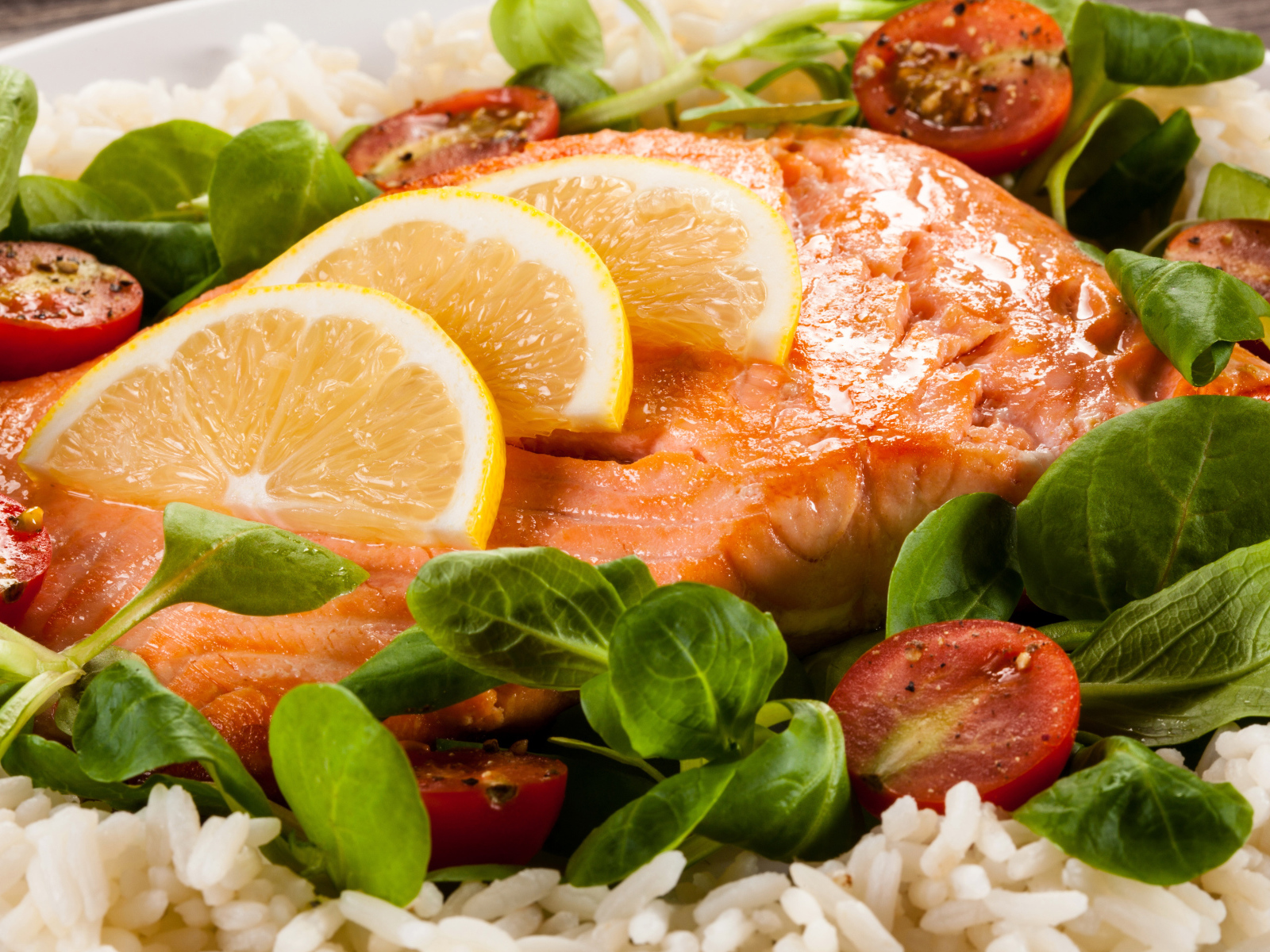 Кусок запеченной красной рыбы на тарелке с лимоном, рисом, базиликом и помидорами