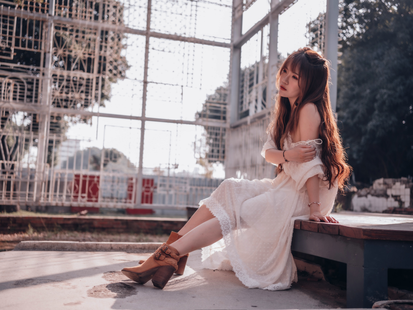 Красивая девушка азиатка в белом платье сидит на лавочке