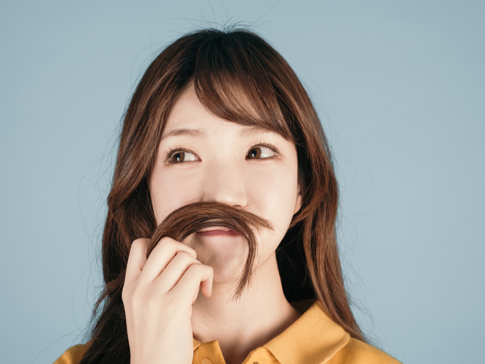 Девушка азиатка закрыла лицо волосами на сером фоне 