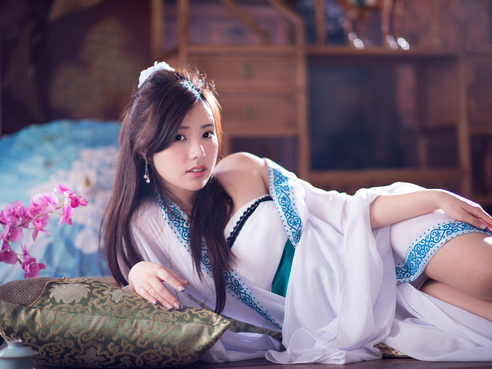 Девушка азиатка в красивом платье лежит на кровати 