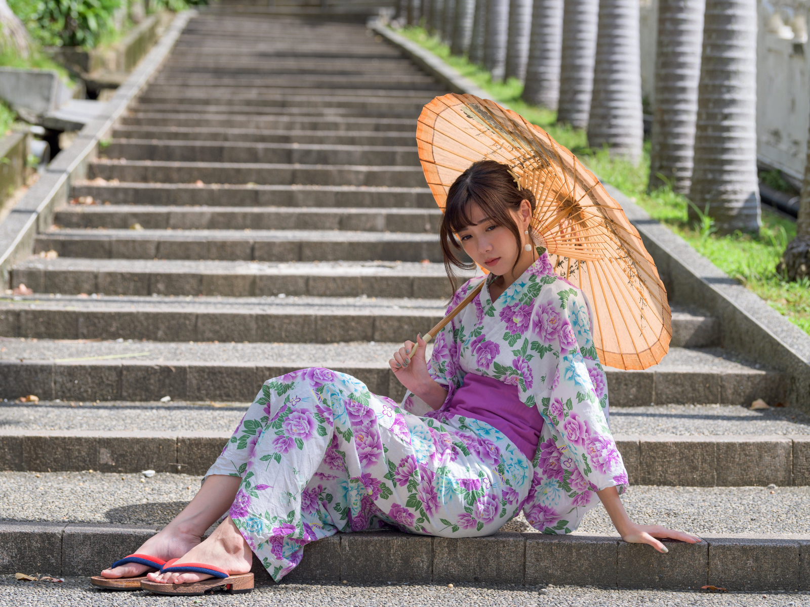 Девушка азиатка в кимоно с зонтом в руках сидит на ступеньках 
