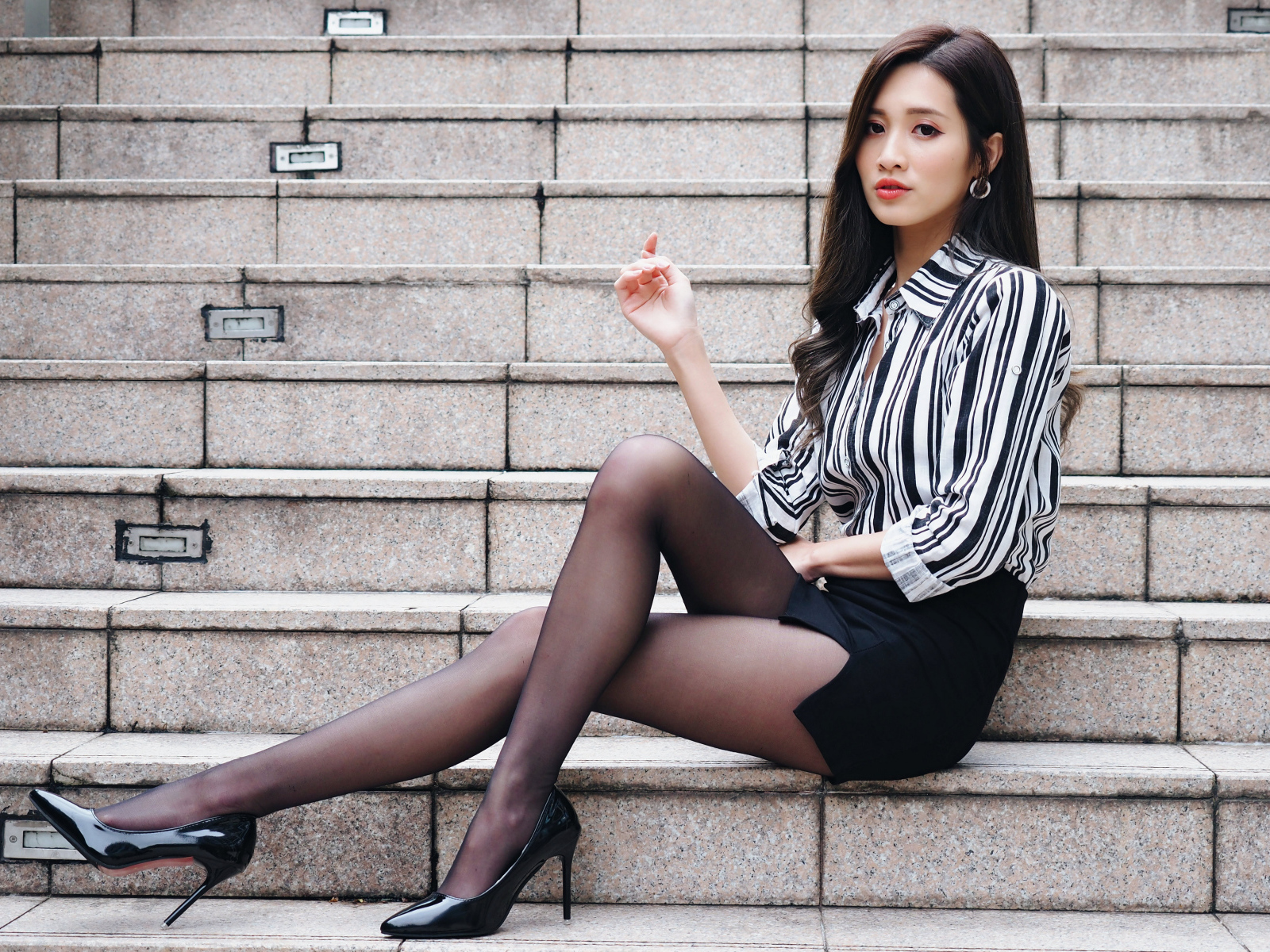 Красивая девушка азиатка в юбке сидит на ступеньках
