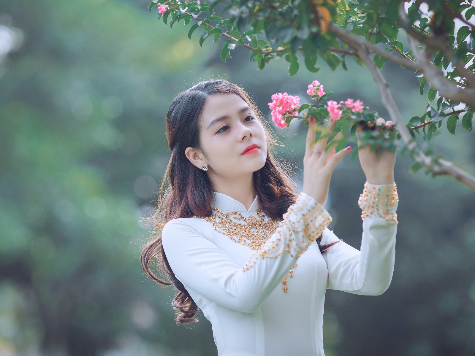 Красивая азиатка в белом платье у ветки с розовыми цветами