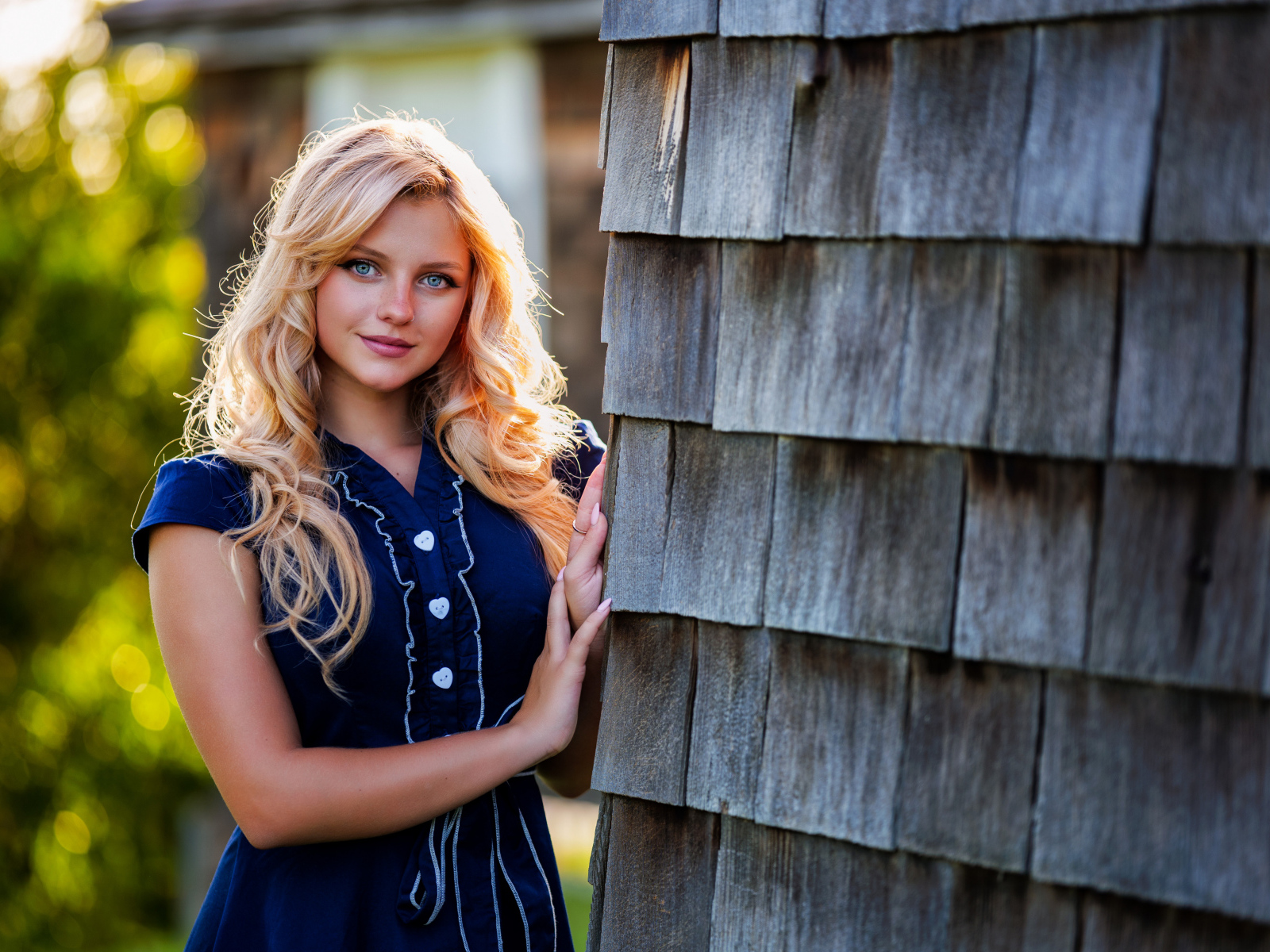 Голубоглазая блондинка в платье стоит у стены 