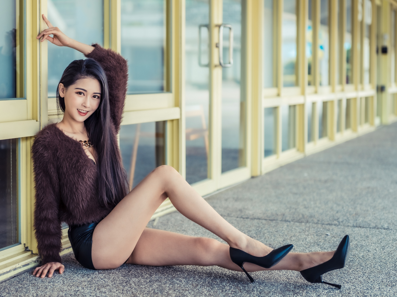 Девушка в свитере сидит у стеклянной стены 