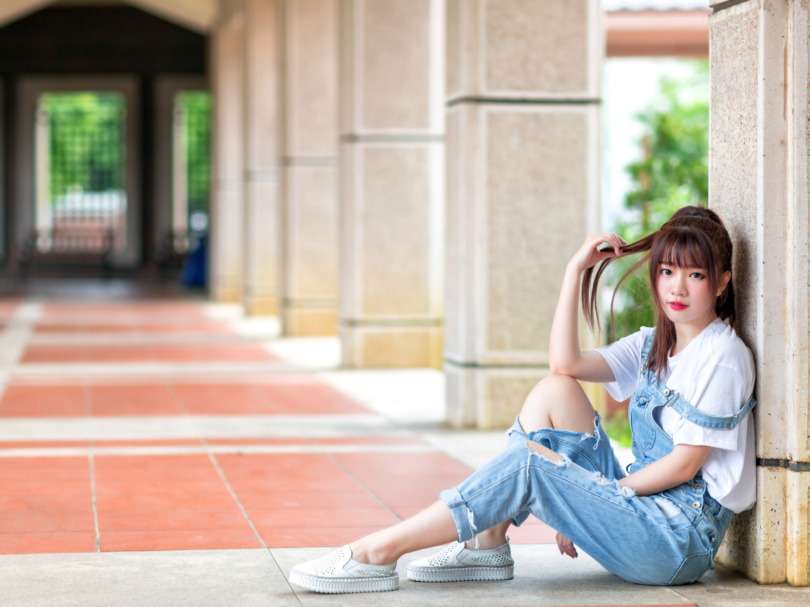 Грустная девушка азиатка сидит у колонны