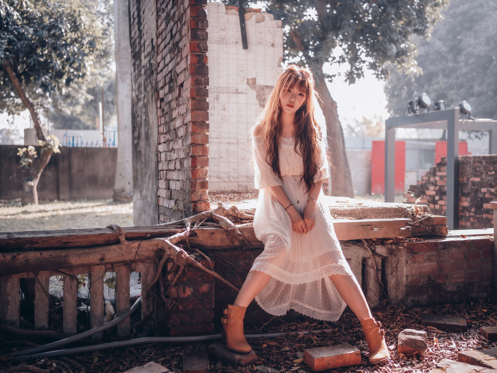 Молодая девушка азиатка в белом платье сидит на разваленной стене