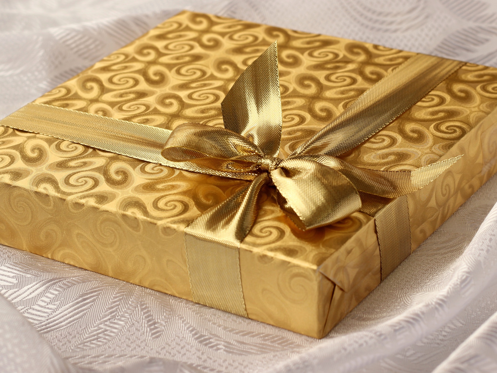 Красивая золотистая коробка с подарком на кровати 