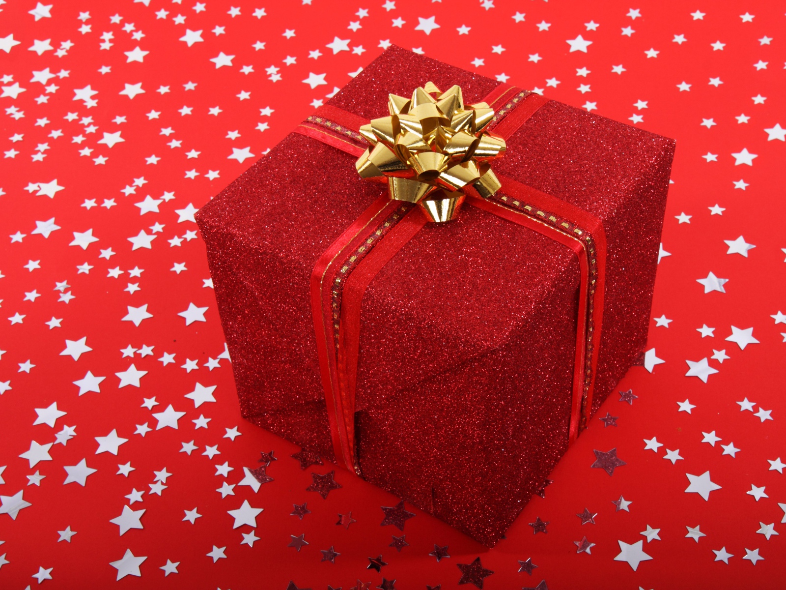 Большой подарок с бантом на красном фоне со звездами 