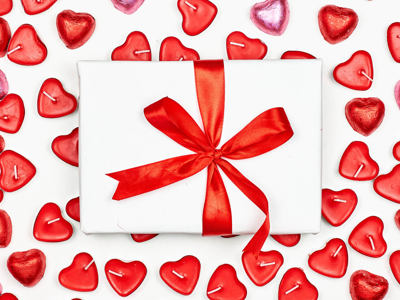 Подарок с красным бантом и свечи в форме сердца на день влюбленных