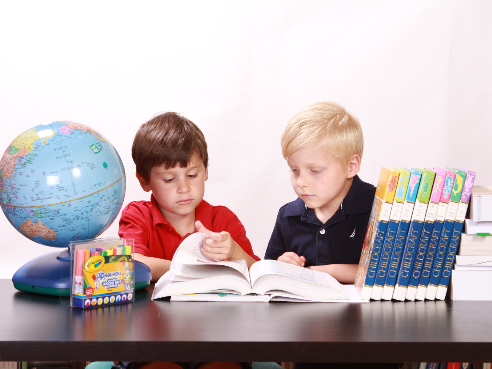 Два мальчика школьника с книгами и глобусом за столом