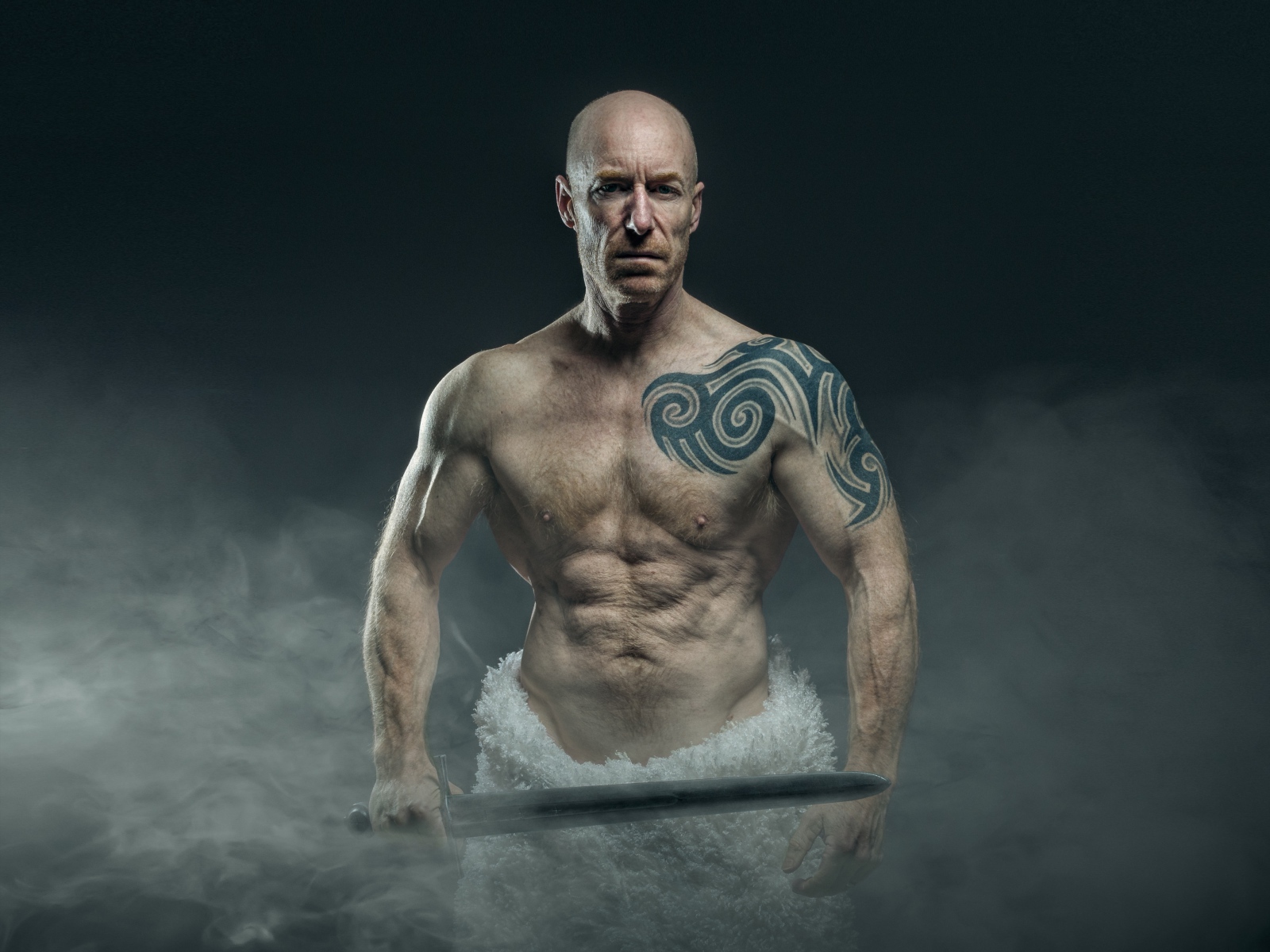 Сильный мужчина с мечом с татуировками на теле 