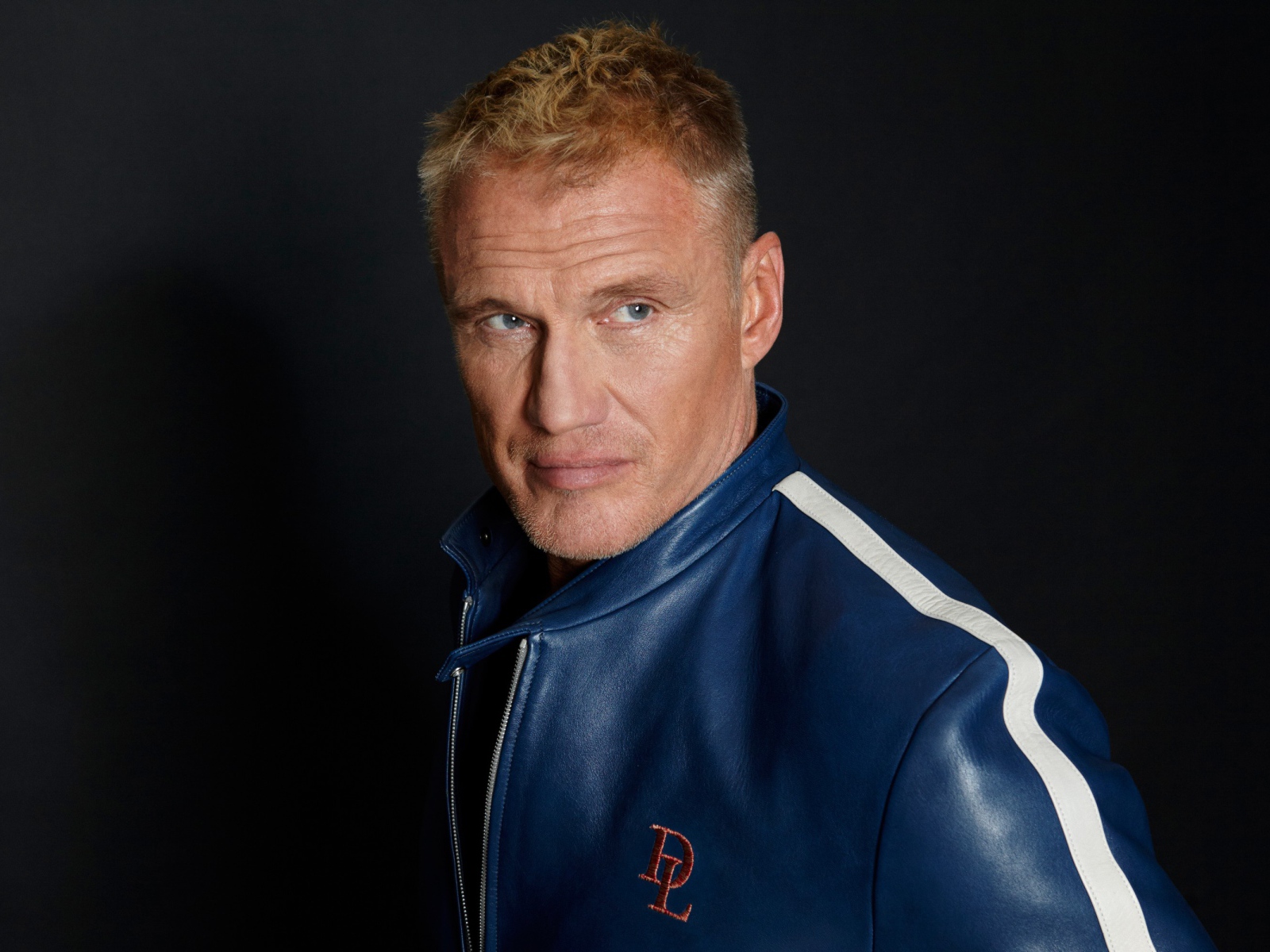 Актер Дольф Лундгрен в куртке на фоне  серой стены