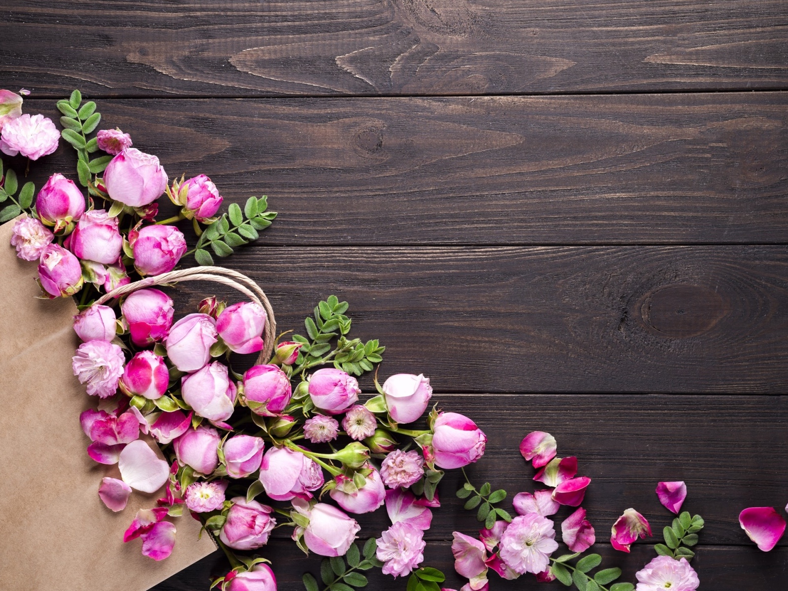 Цветки розовой розы с бумажным пакетом  на деревянном фоне