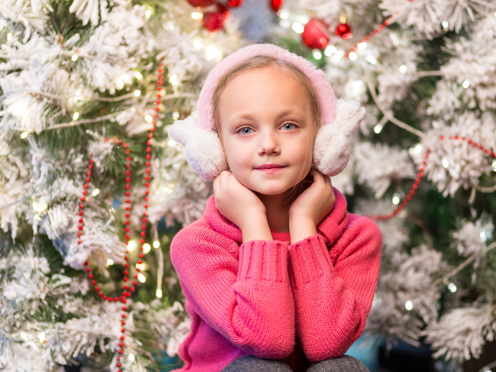 Девочка в розовых наушниках сидит у ели