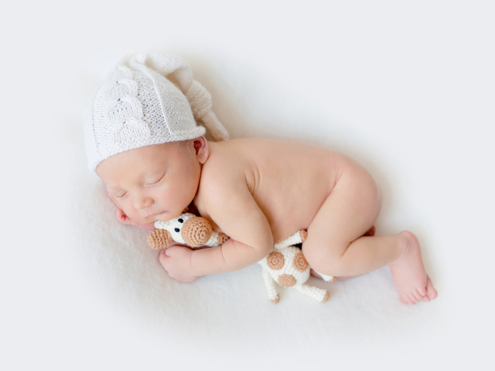 Младенец в шапке с игрушкой на белом фоне