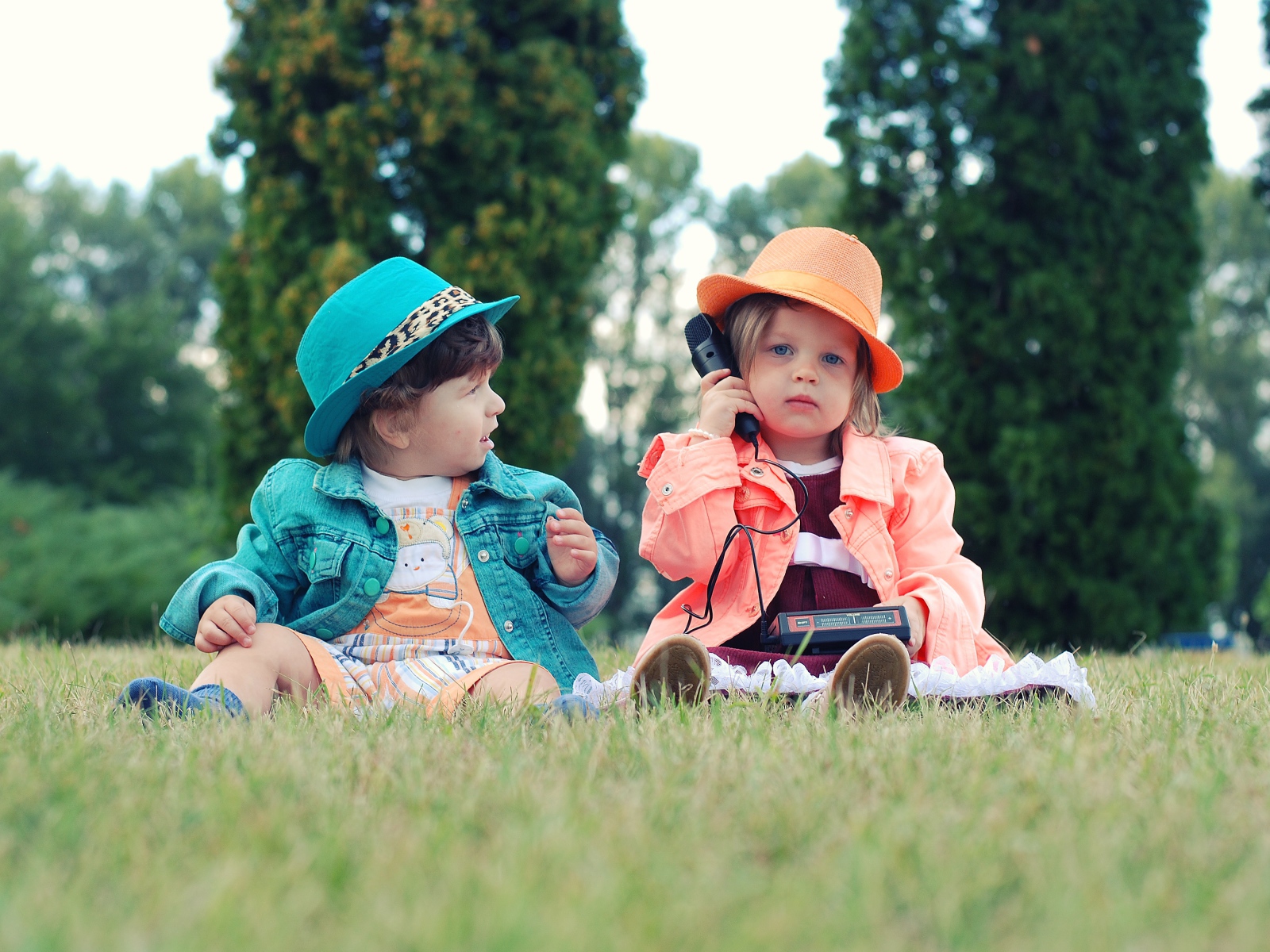 Маленькие девочка и мальчик сидят на траве с телефоном 