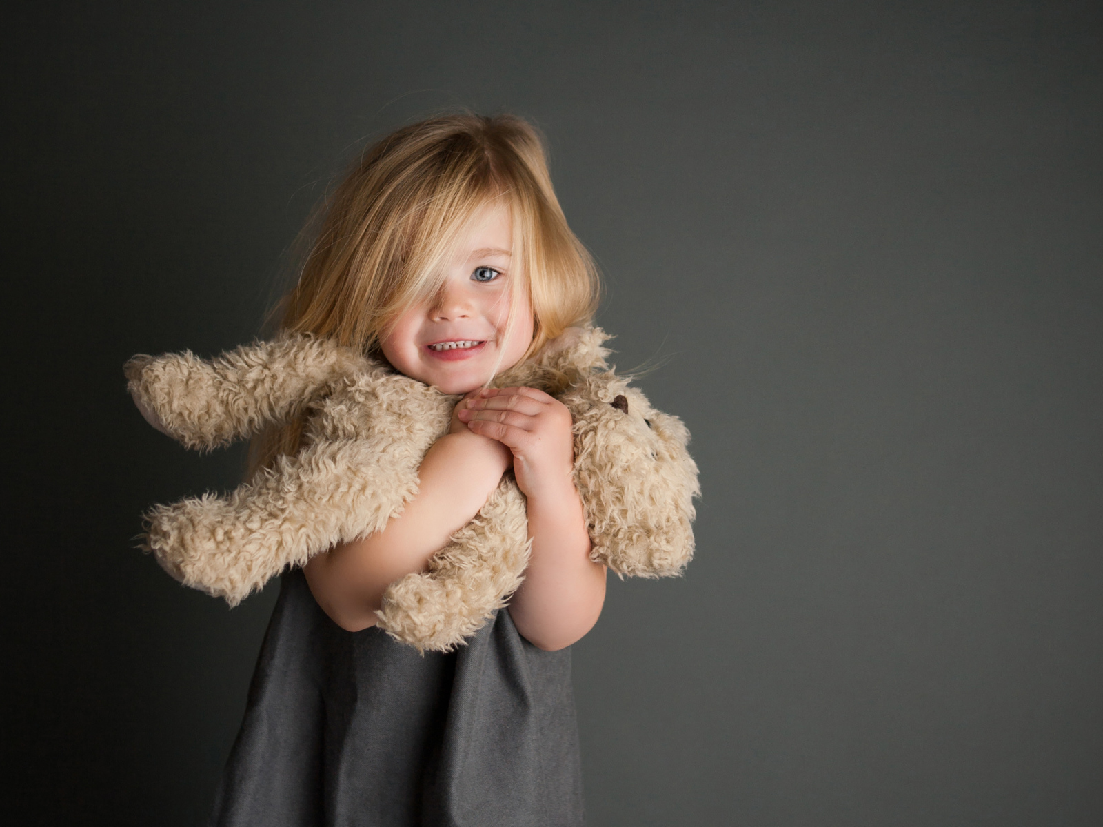 Маленькая девочка с игрушечным медвежонком в руках  на сером фоне 