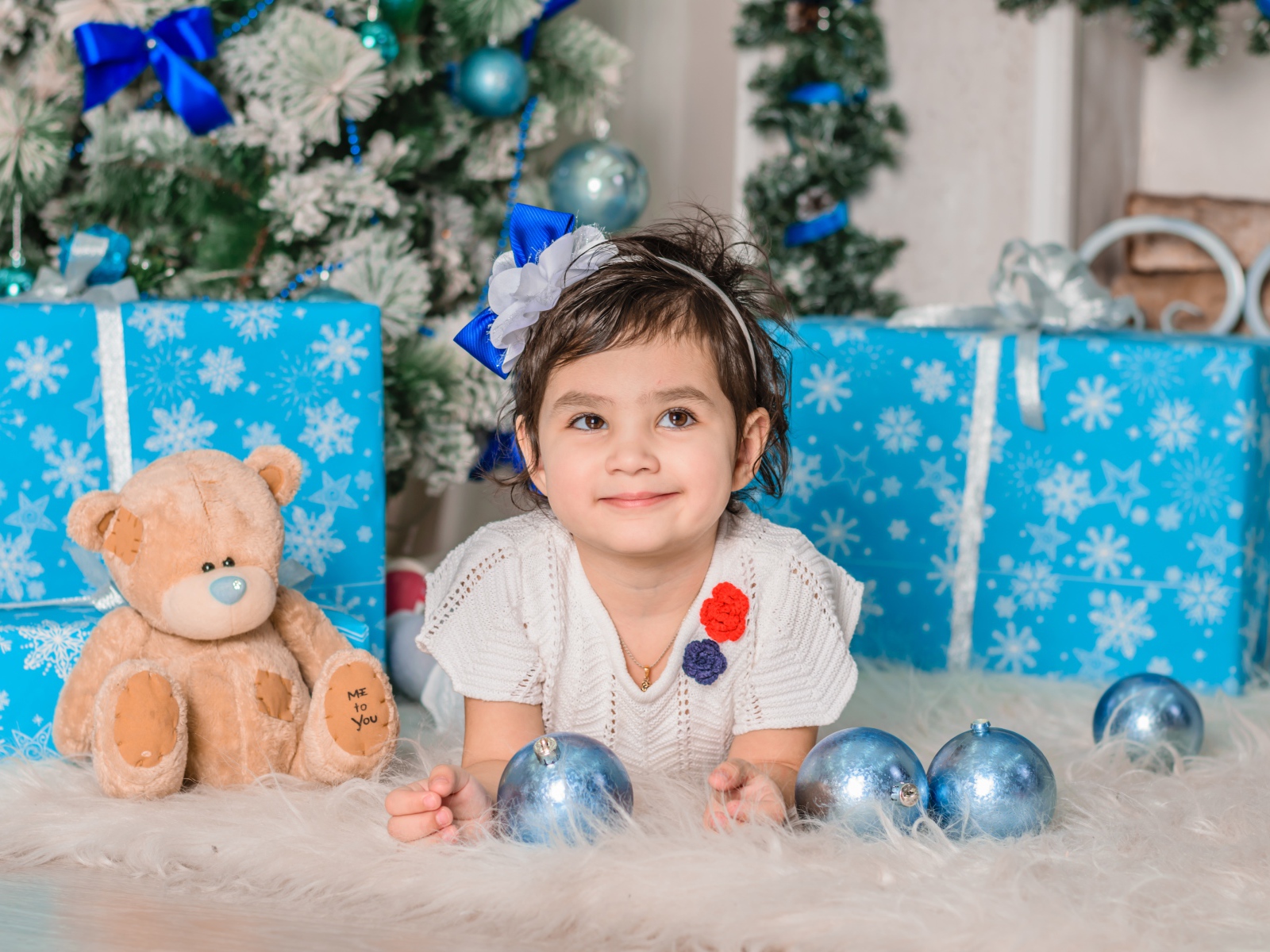 Маленькая девочка с подарками и игрушками под елкой 