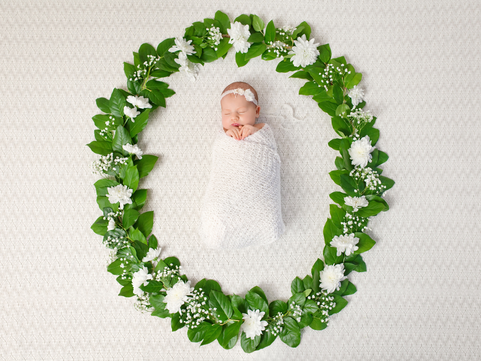 Маленький грудной ребенок спит в зеленом венке из листьев 