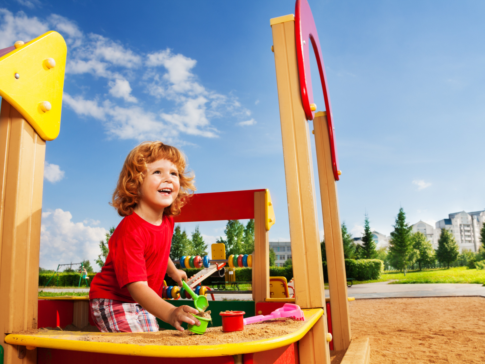 Улыбающийся мальчик в песочнице на детской площадке 
