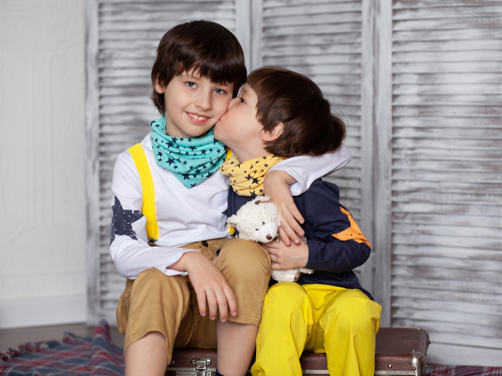 Два маленьких брата сидят на чемодане у стены