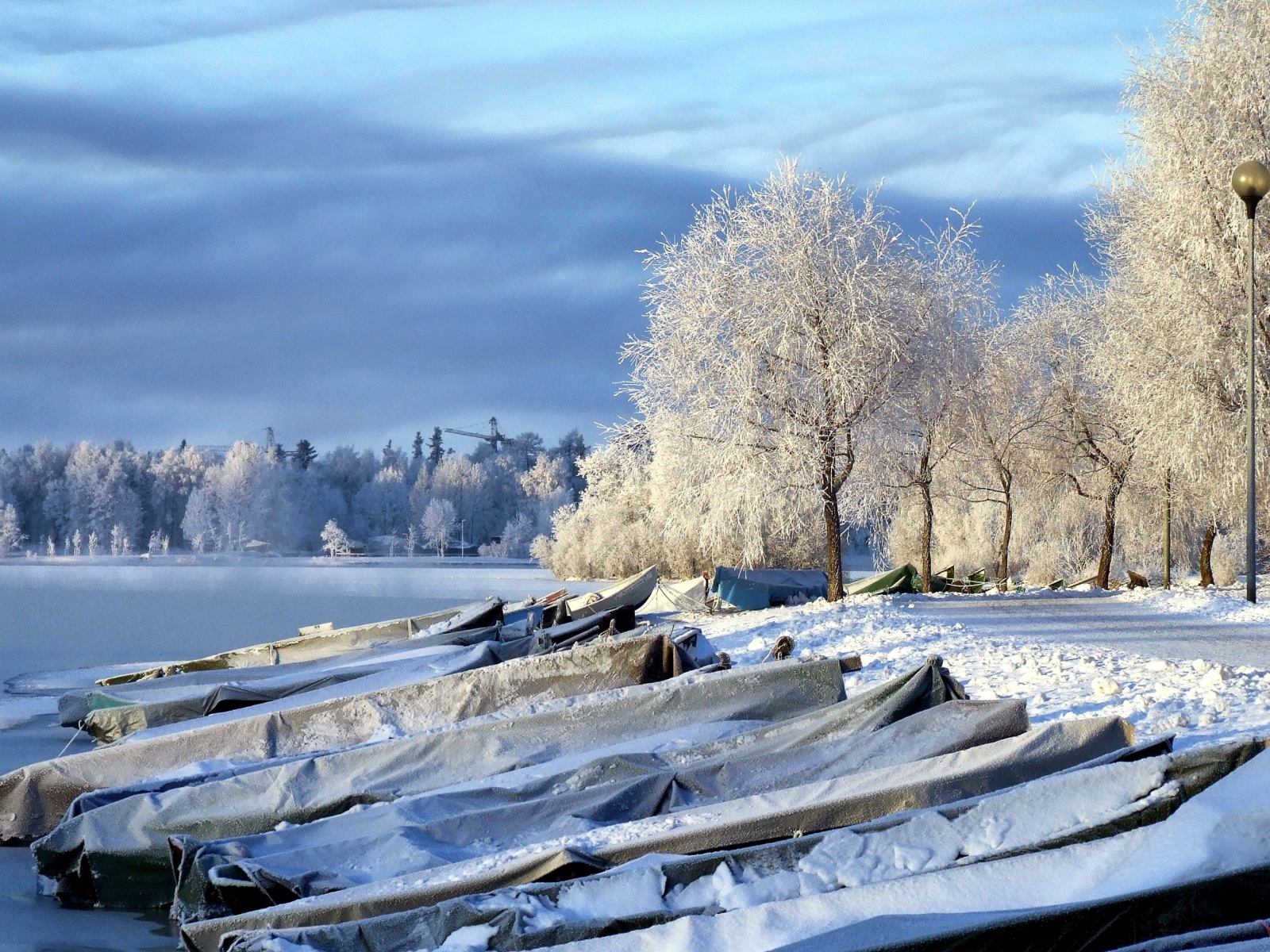 Накрытые лодки на берегу озера зимой
