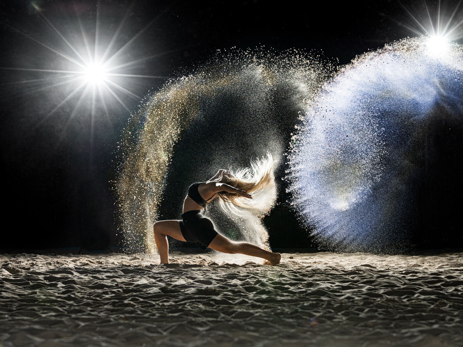 Девушка в черном костюме танцует на песке 