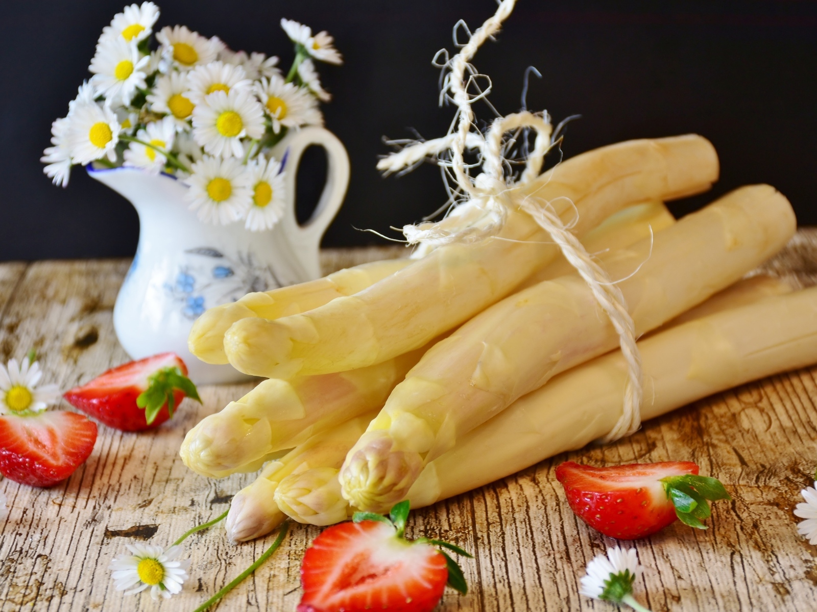 Спаржа на столе с ромашками и ягодами клубники
