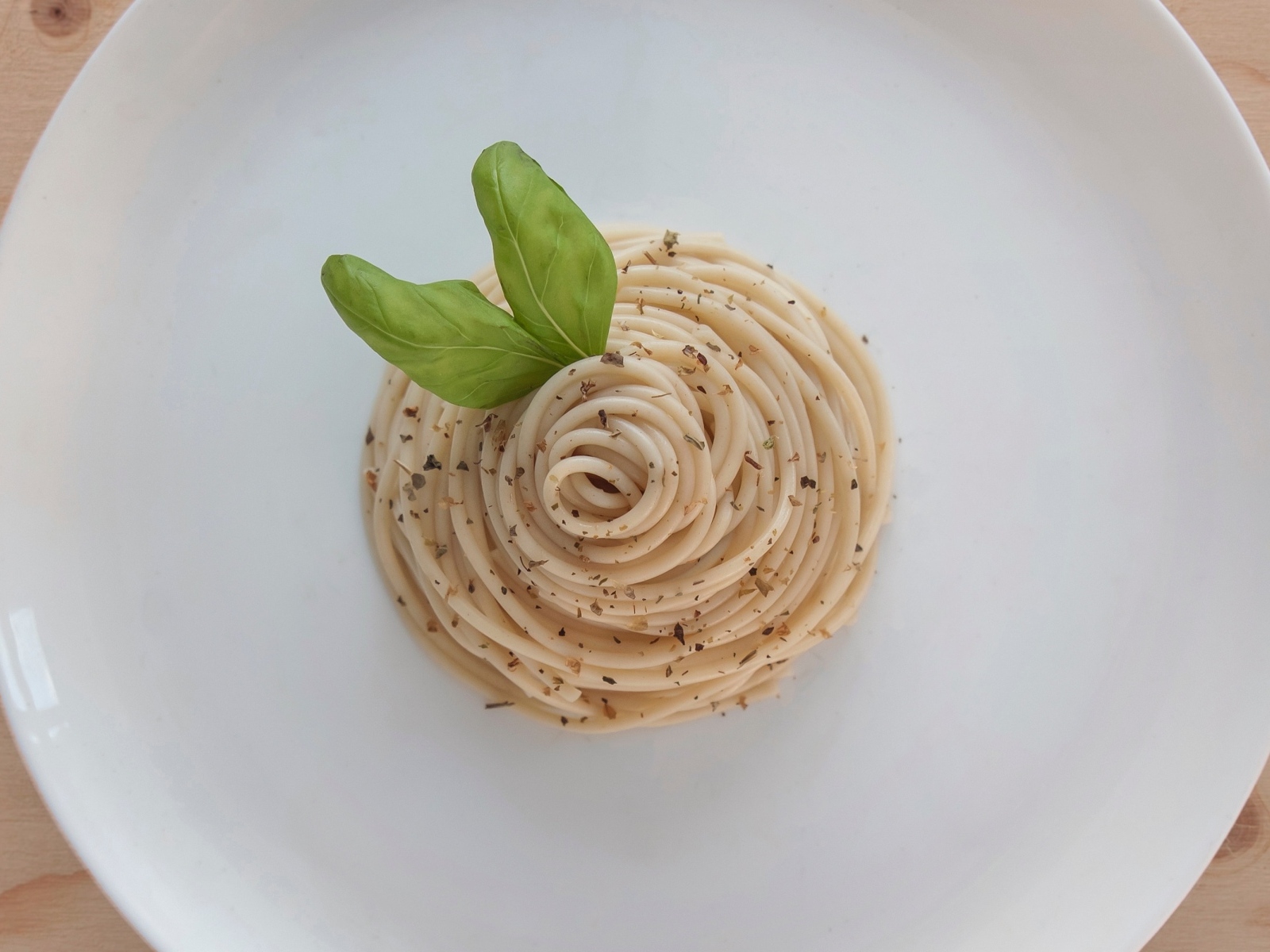 Спагетти с листьями базилика на белой тарелке