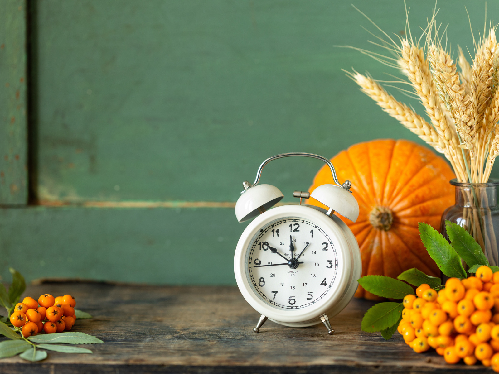 Будильник на столе с тыквой и ягодами рябины
