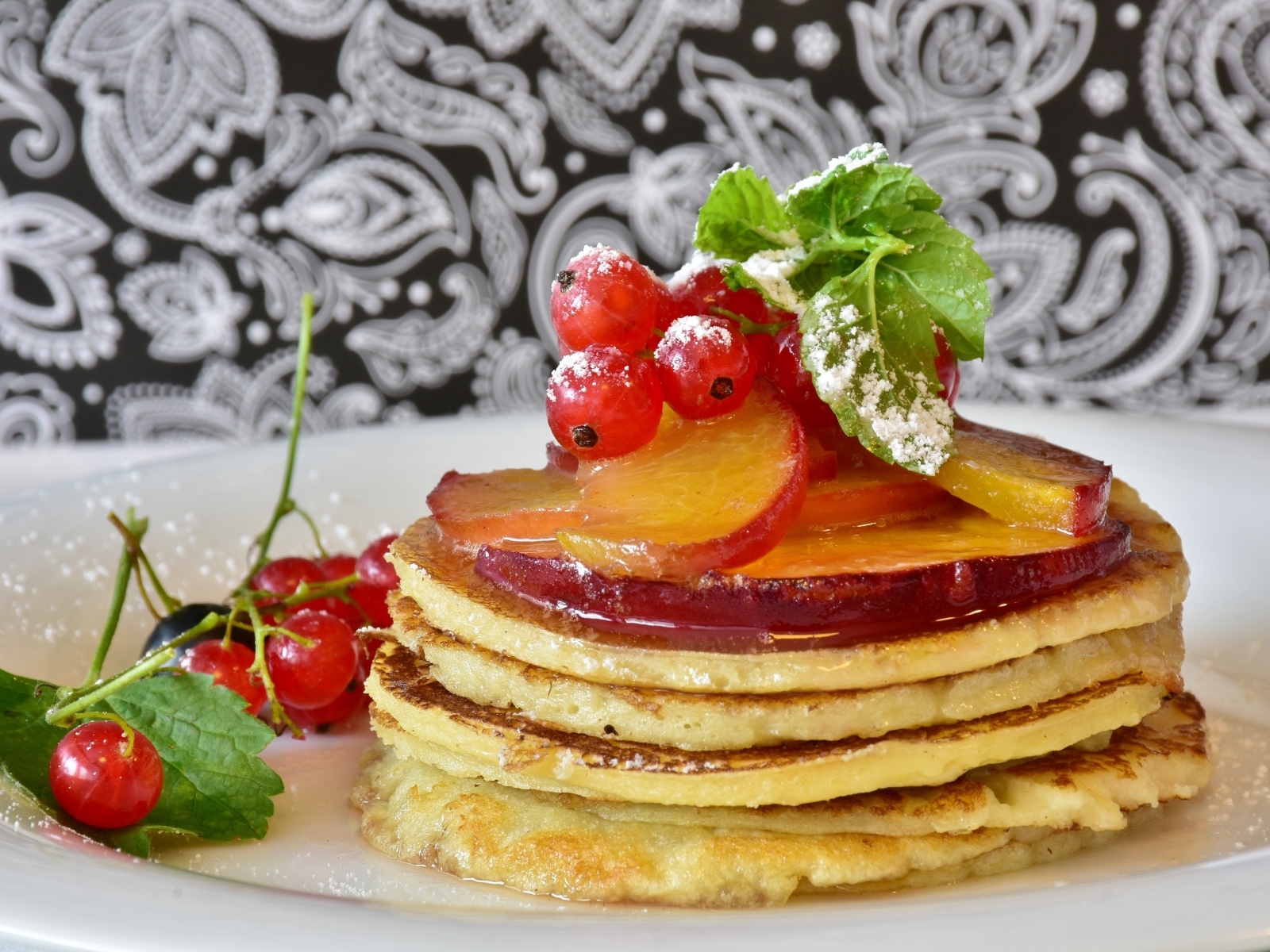 Оладьи на тарелке с ягодами смородины  и сливы