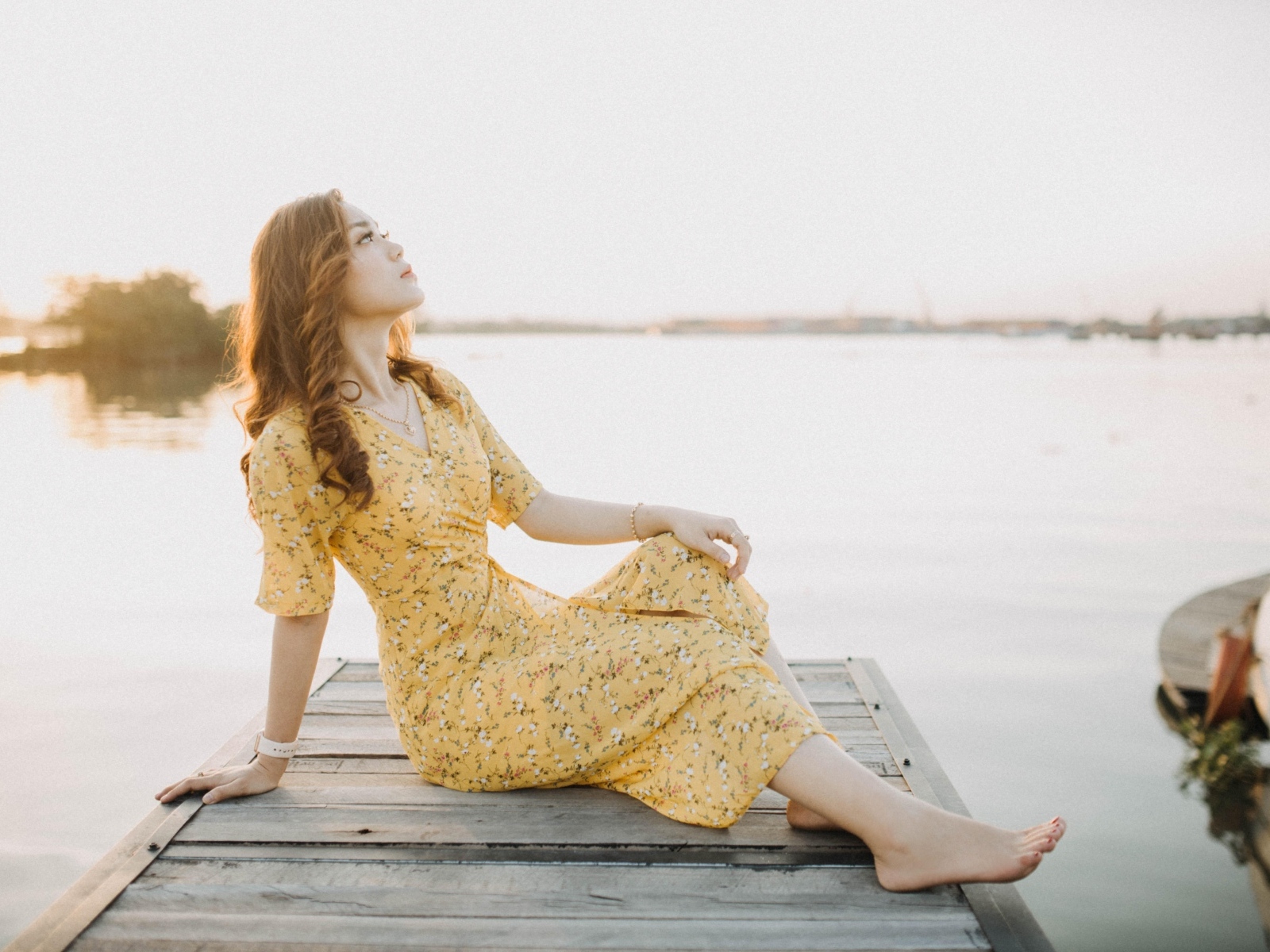 Красивая девушка в платье сидит на мосту у реки