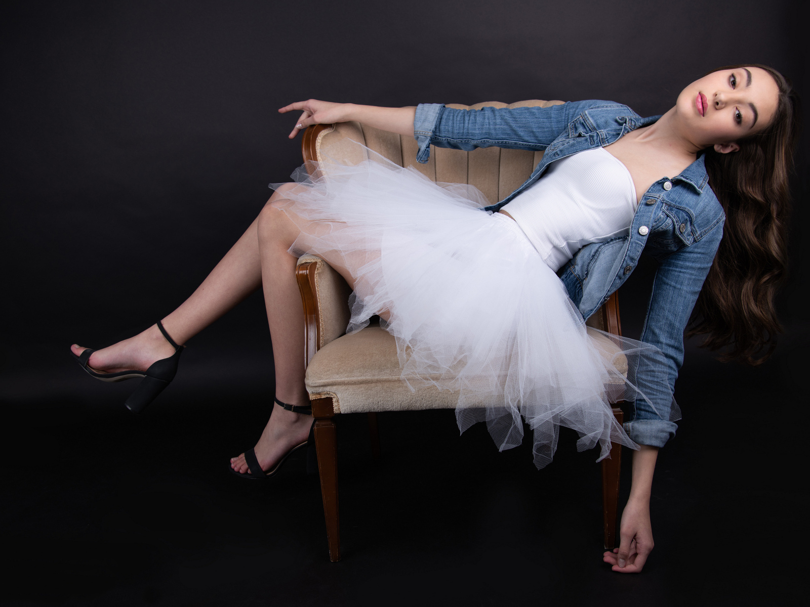 Девушка в белой юбке лежит в кресле на черном фоне