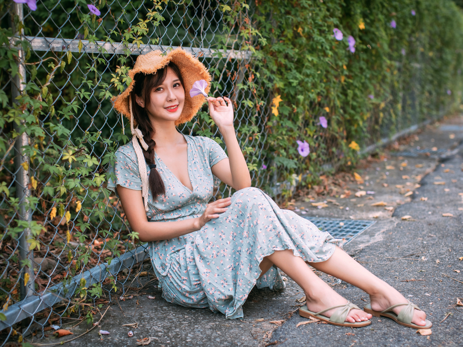 Девушка азиатка в платье сидит у забора
