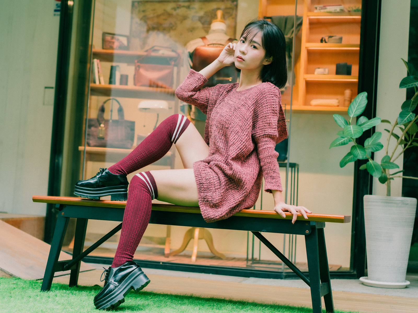 Девушка азиатка в теплом свитере сидит на лавке