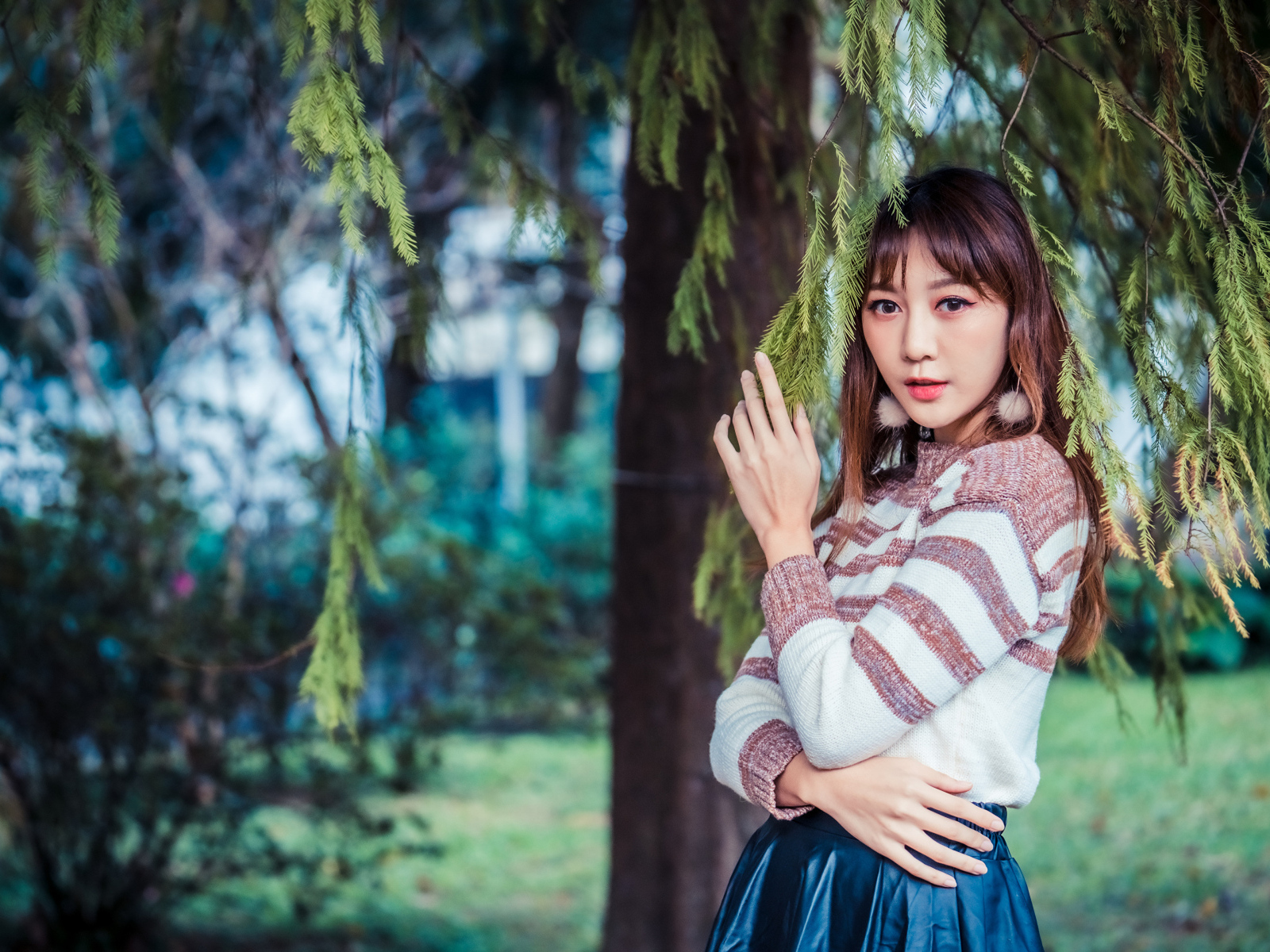 Девушка азиатка стоит у дерева ели