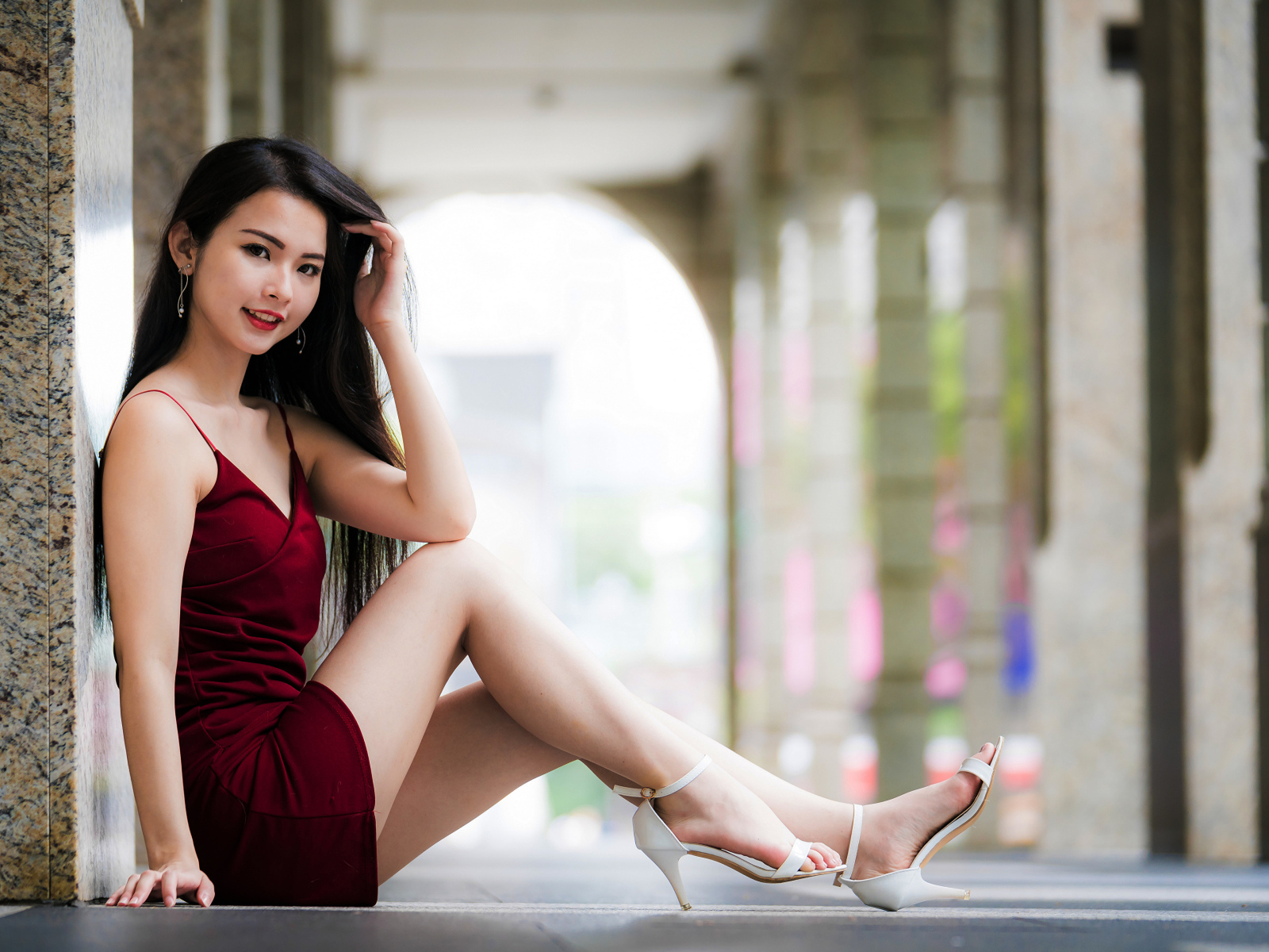 Азиатка в красном платье сидит у стены 