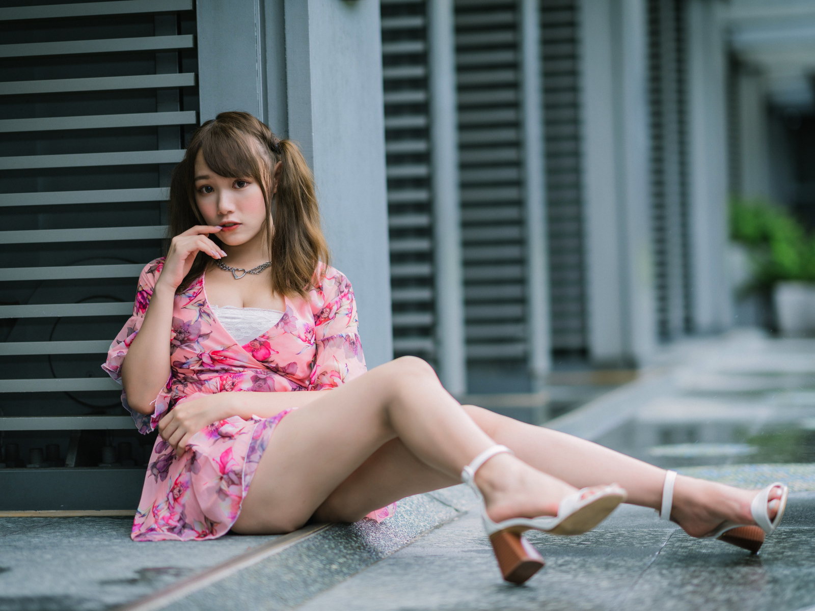 Красивая азиатка в розовом платье сидит у стены