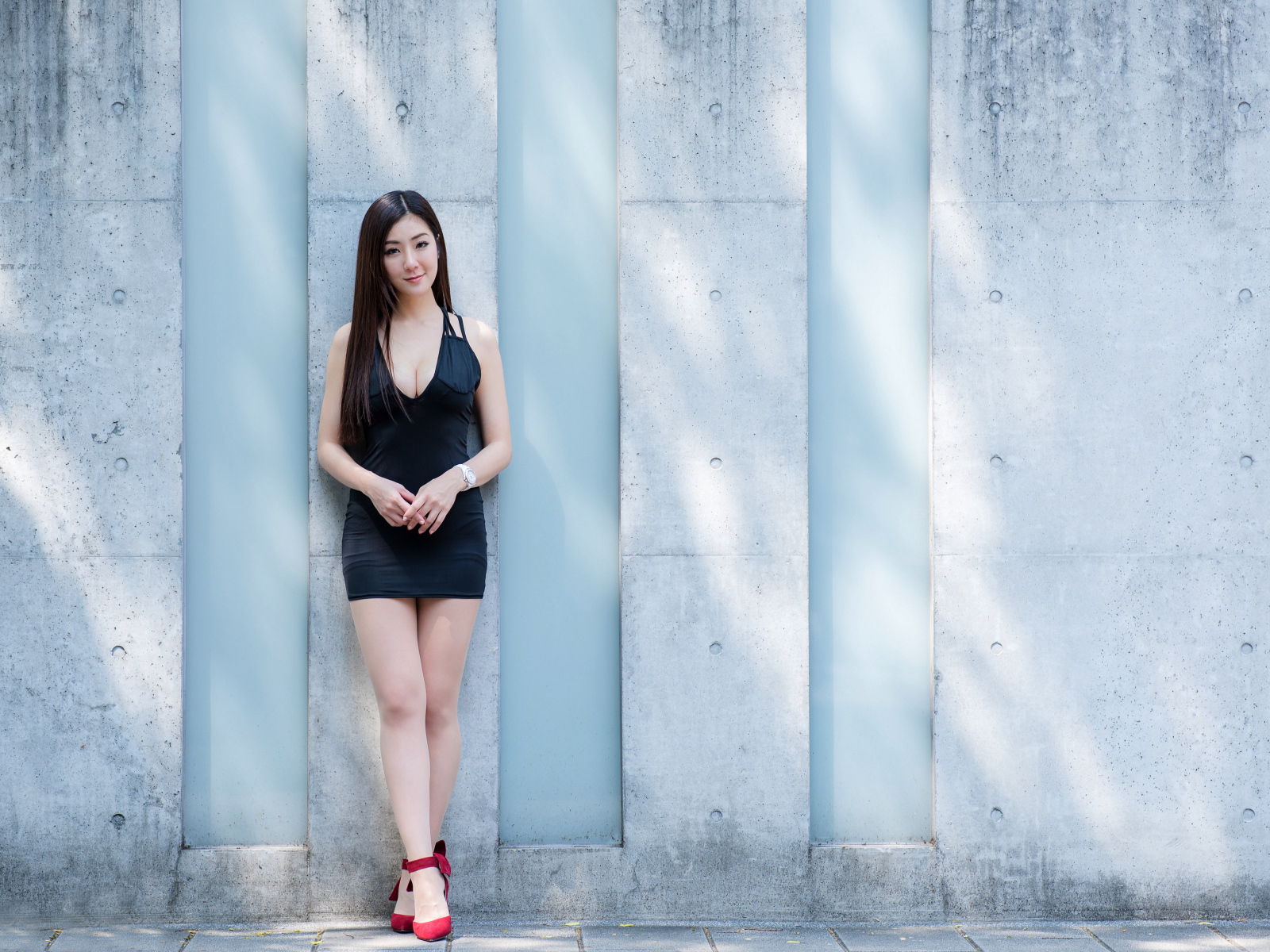 Красивая азиатка в коротком платье стоит у стены