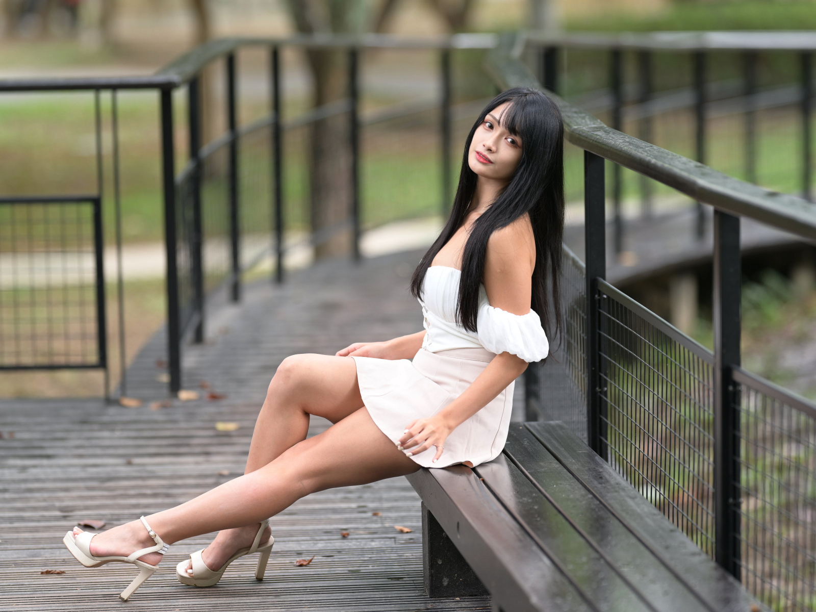 Красивая длинноволосая азиатка в белом платье сидит на лавке