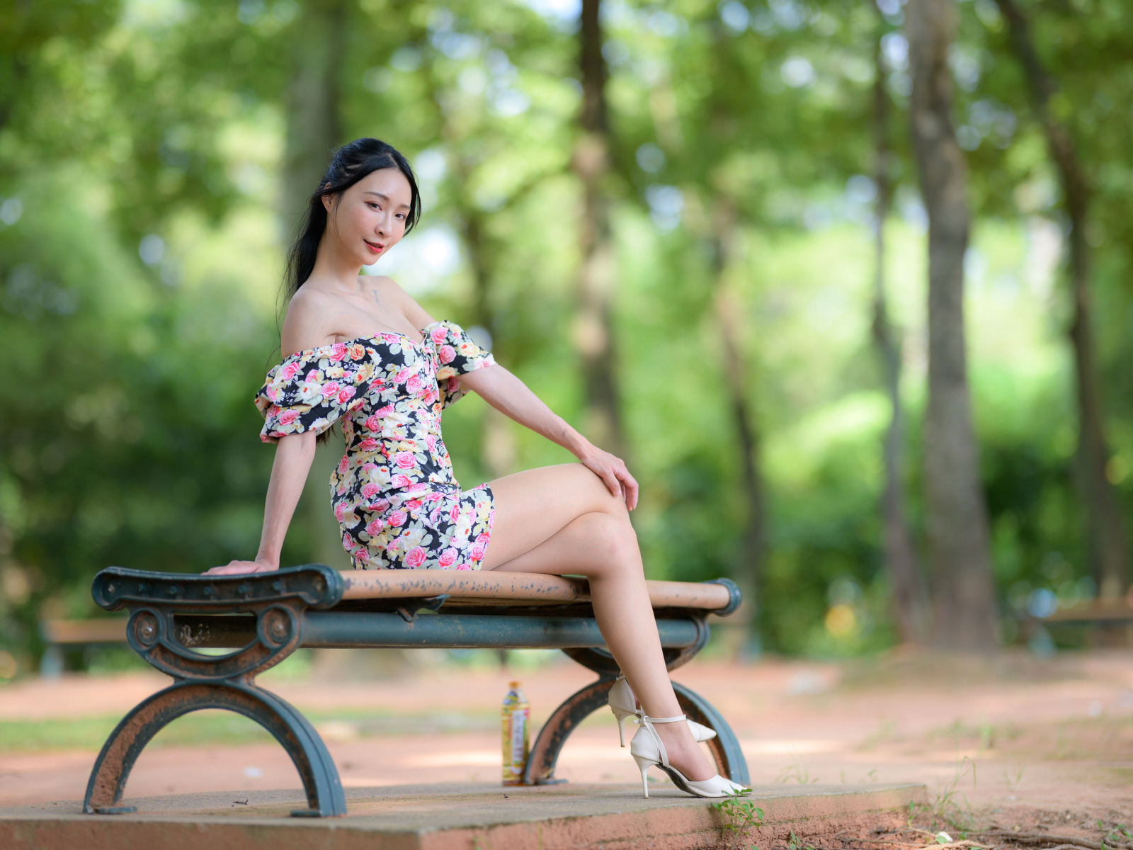 Милая девушка азиатка в платье сидит на лавке в парке