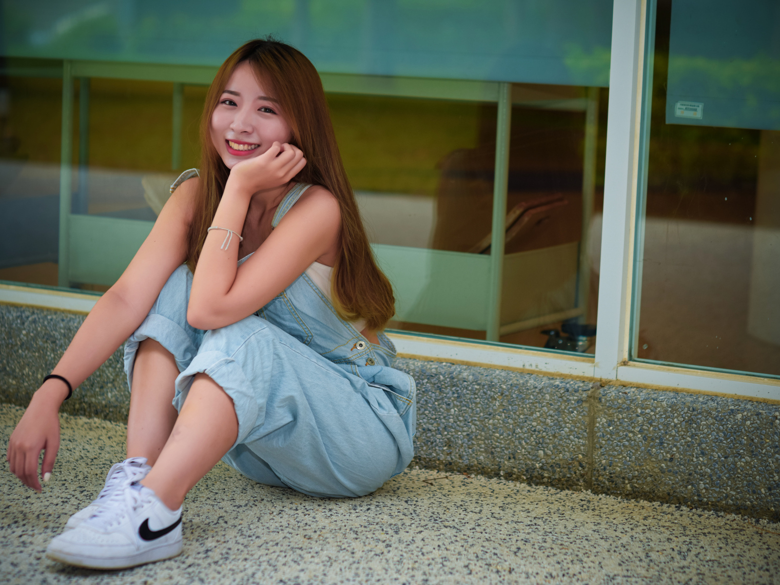 Девушка в джинсовом комбинезоне сидит на полу