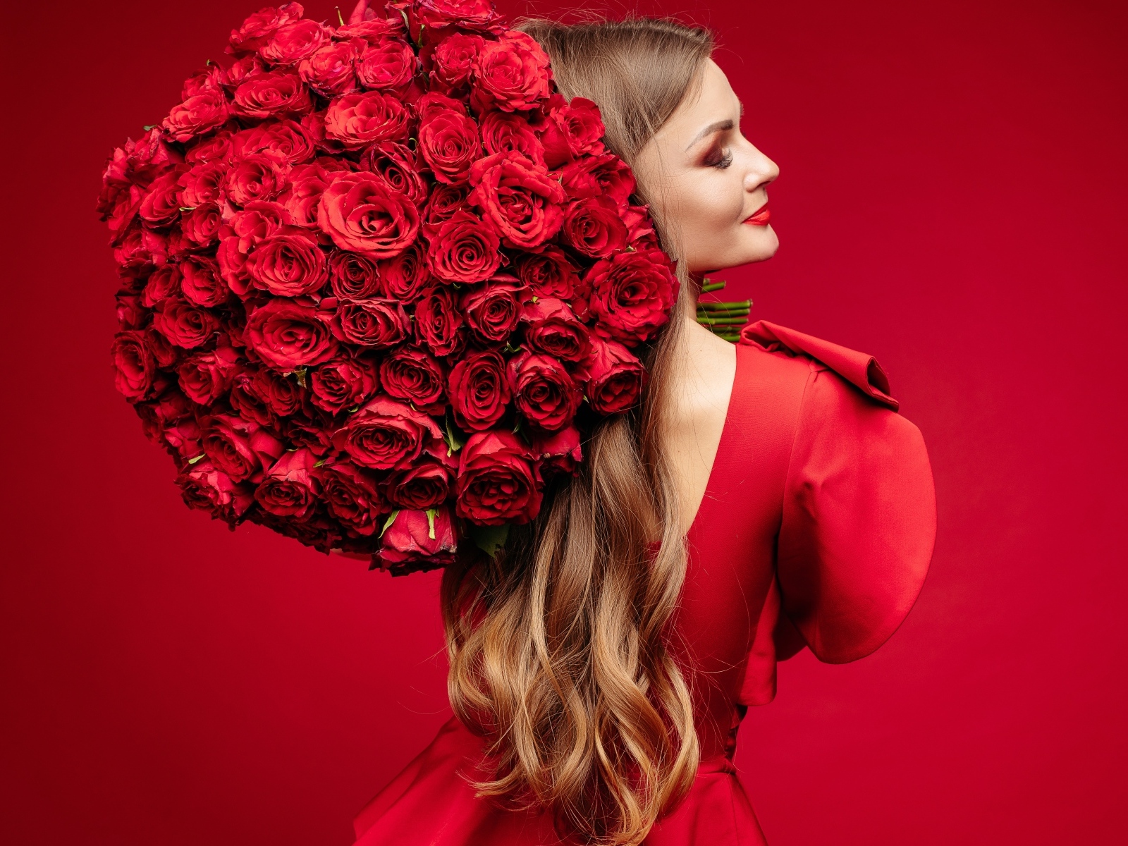 Девушка с большим букетом красных роз на красном фоне
