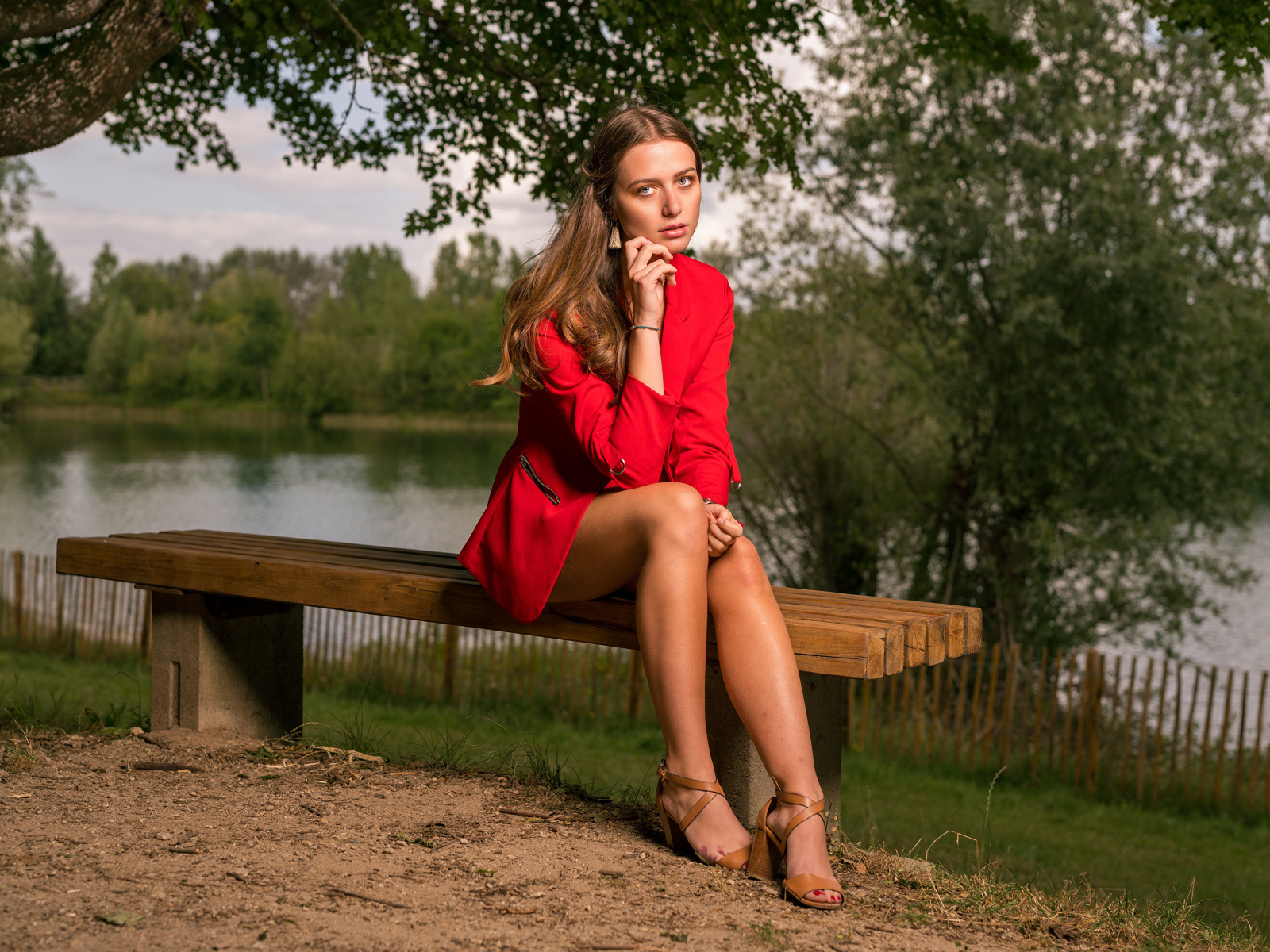 Грустная девушка в красном пальто сидит на лавке